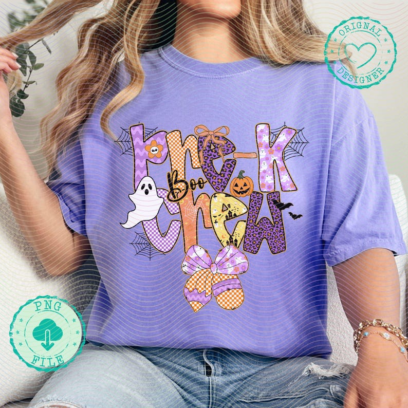 May include: A light purple t-shirt with the words "Boo Crew" in a Halloween-themed design. The design includes a ghost, pumpkin, spiderwebs, and bows. The shirt is a relaxed fit.