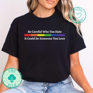 May include: Black t-shirt with the text "Be Careful Who You Hate, It Could Be Someone You Love" in white. The text is above a rainbow-colored stripe. The shirt has a round neckline and short sleeves.