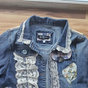 May include: A blue denim jacket with white lace trim and patchwork details. The jacket has a label that reads "Delicious Label".