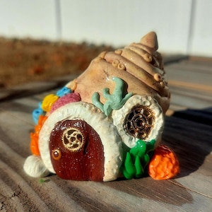 May include: A whimsical seashell house with a brown door, white trim, and colorful accents. The house is decorated with green seaweed and orange coral.
