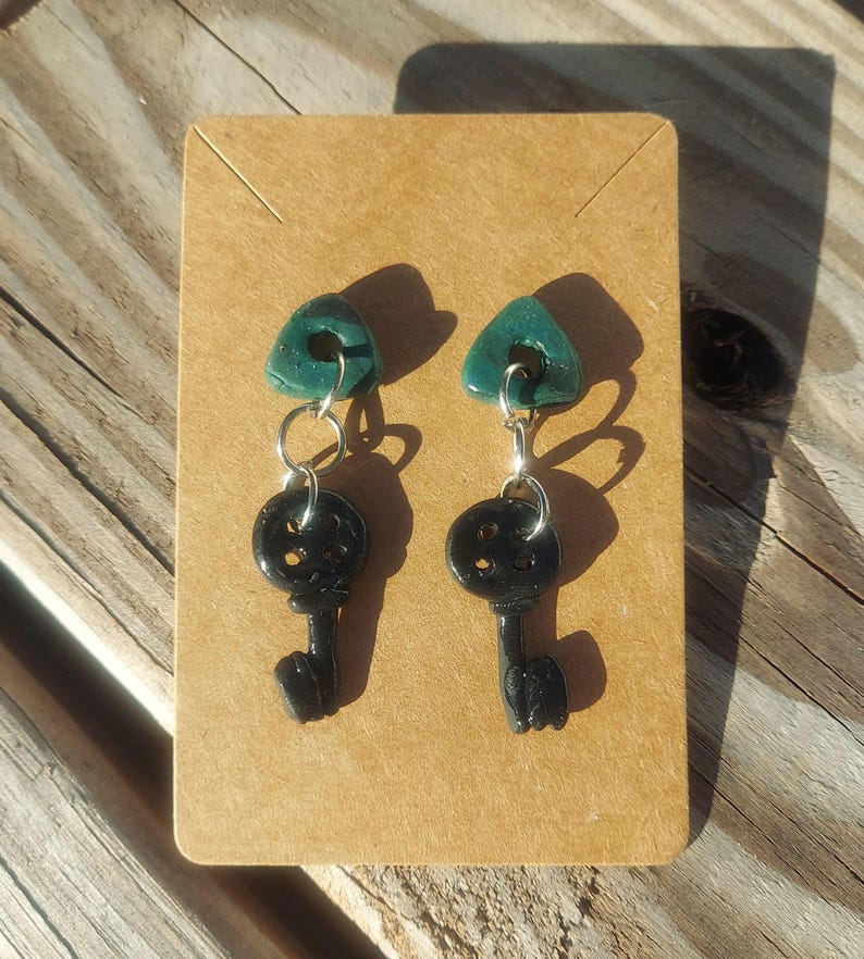May include: A pair of earrings featuring black key-shaped charms with a circle detail and teal triangle charms with a hole in the center.