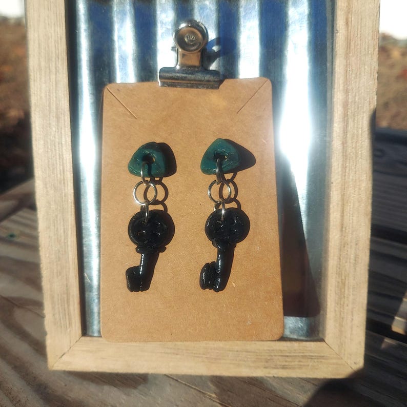 May include: A pair of dangle earrings with black key charms and green triangle-shaped tops.