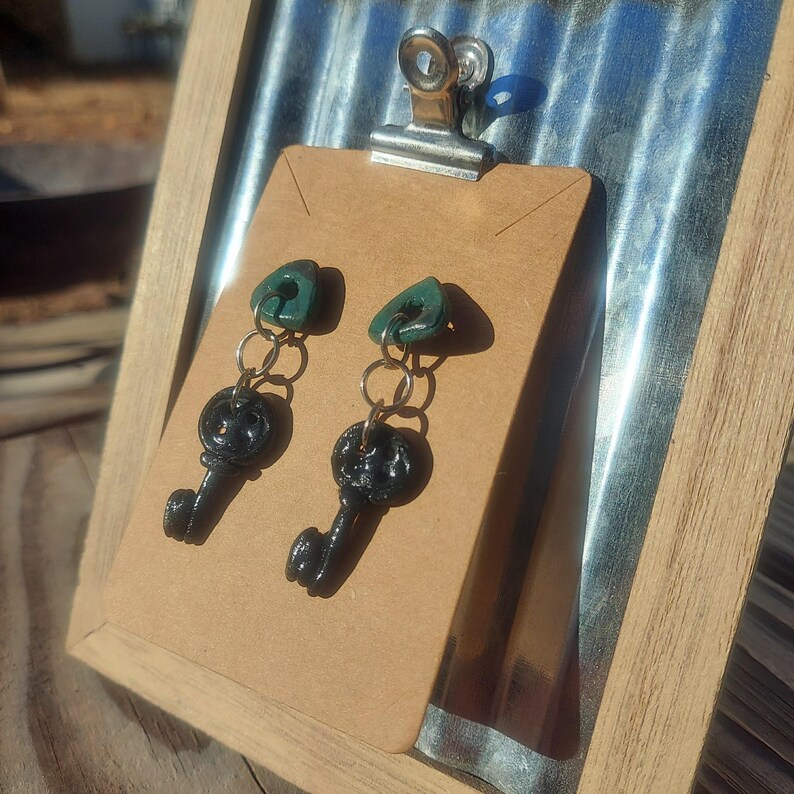 May include: A pair of black key-shaped earrings with green triangle charms hanging from silver chains.