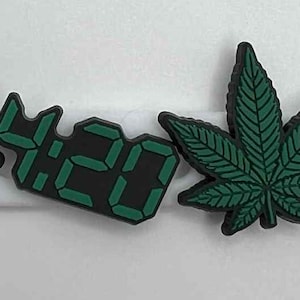 May include: Four shoe charms featuring cannabis leaf designs, the number "4:20", and the text "EAT SLEEP SMOKE REPEAT". The charms are green and black, set against a white background.