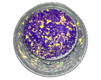 Puede incluir: Un tarro de cristal transparente lleno de purpurina morada y amarilla. La purpurina es una mezcla de pequeñas formas irregulares, creando un efecto brillante. El tarro tiene un diseño decorativo grabado alrededor del borde.