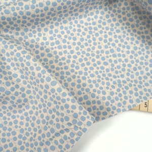 Puede incluir: Una tela beige con un patrón de lunares azul claro. La tela está doblada y se puede ver una cinta métrica en la esquina inferior derecha.