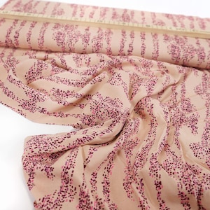 Peut inclure: Tissu de couleur pêche avec un imprimé abstrait rose et violet. Le tissu a une texture douce et fluide.