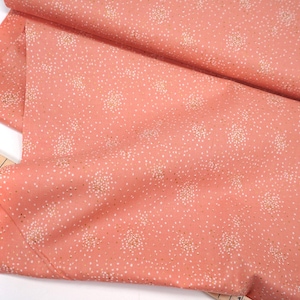Peut inclure: Un tissu de couleur pêche avec un motif floral blanc. Le tissu est plié en deux et un mètre ruban est visible en bas à gauche.