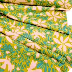 Può includere: Un tessuto giallo con un motivo floreale rosa e turchese. Il tessuto è piegato e ha una texture morbida e fluida.