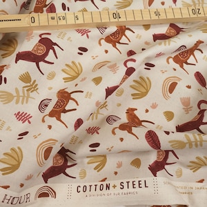 Op de afbeelding: Beige katoenen stof met een herhalend patroon van gestileerde paarden, bladeren en abstracte vormen in tinten bruin, rood en geel. De stof heeft de tekst "Majestic Hour" en "Cotton + Steel" erop gedrukt.