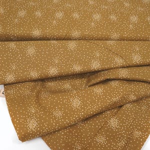 Peut inclure: Un tissu jaune moutarde avec un motif de confettis blancs. Le tissu est plié et une règle est visible en arrière-plan.