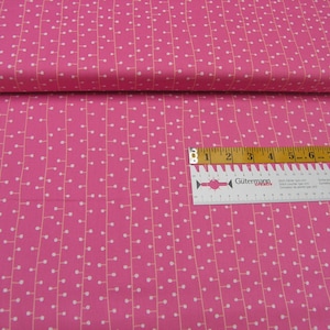 Peut inclure: Tissu rose avec un motif blanc répétitif de petits cercles reliés par de fines lignes. Une règle est placée sur le tissu, montrant une mesure de 23 cm.