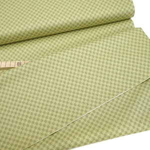 Könnte beinhalten: Ein grüner Stoff mit einem sich wiederholenden Muster aus kleinen, hellgelben Kreisen. Der Stoff ist in der Mitte gefaltet und ein Holzlineal liegt auf der Falte.