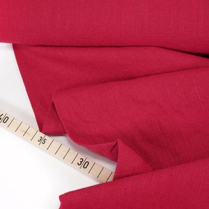 Könnte beinhalten: Roter Leinenstoff, der auf einer weißen Oberfläche gefaltet ist, mit einem hölzernen Maßband, das in Zentimetern gekennzeichnet ist. Das Band zeigt 30, 35, 40 und 45 an.