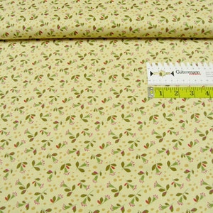 Könnte beinhalten: Ein beigefarbener Stoff mit einem sich wiederholenden Muster aus kleinen grünen Blättern und roten Blüten. Der Stoff ist in der Mitte gefaltet und ein Maßband liegt darauf.