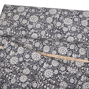 Peut inclure: Un tissu bleu marine avec un motif floral blanc. Le tissu est plié et surmonté d'un mètre ruban et d'une bobine de fil.