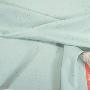 Peut inclure: Un tissu en coton bleu clair avec un imprimé d'étoiles dorées. Le tissu est plié et porte une étiquette blanche avec le mot "COTTON" imprimé dessus.