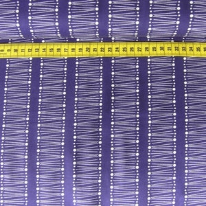 Peut inclure: Tissu violet avec un motif géométrique blanc composé de lignes et de points. Le tissu est mesuré avec un mètre ruban jaune.