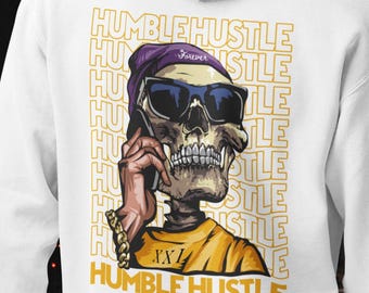 May include: A white hooded sweatshirt featuring a graphic on the back of a skull wearing a purple beanie and sunglasses, talking on a cell phone. The skull wears a yellow shirt with the text XXI and the words HUMBLE HUSTLE in yellow.