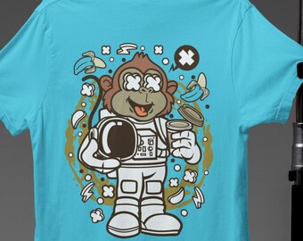 May include: A turquoise blue t-shirt with a cartoon illustration of a monkey astronaut holding a cup of coffee. The monkey is wearing a white space suit and has a surprised expression on its face. The background is filled with bananas, coffee beans, and other space-themed elements.