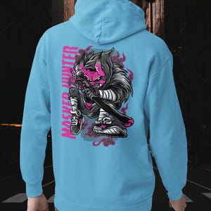 May include: A light blue hooded sweatshirt featuring a graphic on the back of a stylized character with a pink mask and horns, holding a sword. The text "MASKED HUNTER" is printed vertically in pink next to the character, surrounded by pink flames.