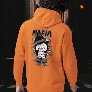 May include: An orange hooded sweatshirt featuring a graphic on the back of a gorilla wearing a black fedora hat and a bow tie with a cigar in its mouth. The word MAFIA is printed in black above the gorilla, surrounded by grey paint splatter.
