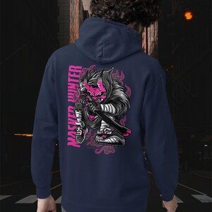 May include: A navy blue hooded sweatshirt featuring a graphic on the back of a stylized character with a pink mask and horns, holding a sword. The text "MASKED HUNTER" is printed vertically in pink next to the character, surrounded by pink flames.