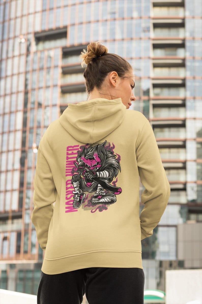 May include: A beige hooded sweatshirt featuring a graphic on the back of a stylized character with a pink face and dark hair holding a sword. The text "MASTER HUNTER" is printed vertically in pink next to the character, surrounded by purple smoke.