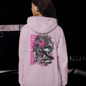 May include: A light purple hooded sweatshirt featuring a graphic on the back of a stylized creature with pink skin, horns, and dark fur, holding a sword. The text "MASKED HUNTER" is printed vertically in pink next to the illustration.