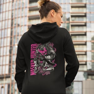 May include: A black hooded sweatshirt featuring a graphic on the back of a stylized character with a pink mask and dark fur, holding a sword. The text MASHED HUNTER is printed vertically in pink next to the character, surrounded by pink smoke.