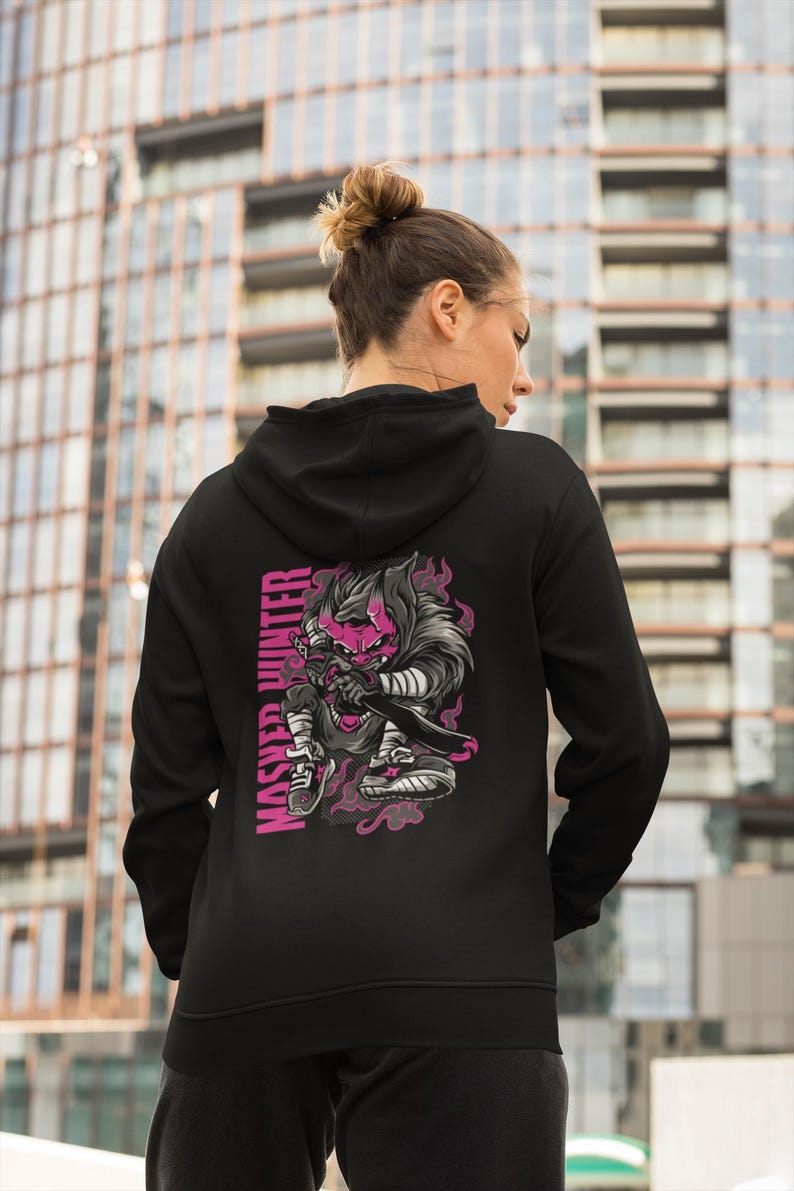 May include: A black hooded sweatshirt featuring a graphic on the back of a stylized character with a pink mask and dark fur, holding a sword. The text MASHED HUNTER is printed vertically in pink next to the character, surrounded by pink smoke.