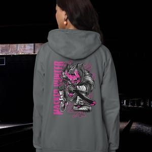 May include: A charcoal gray hooded sweatshirt featuring a graphic on the back of a pink-skinned, horned creature holding a sword. The text MASKED HUNTER is printed vertically in pink next to the illustration, which includes pink smoke accents.