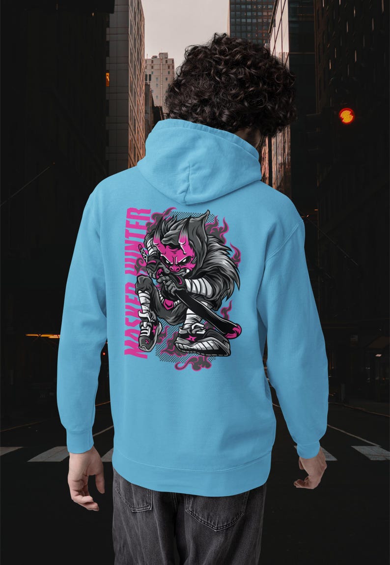 May include: A light blue hooded sweatshirt featuring a graphic on the back of a stylized character with a pink mask and horns, holding a sword. The text "MASKED HUNTER" is printed vertically in pink next to the character, surrounded by pink flames.