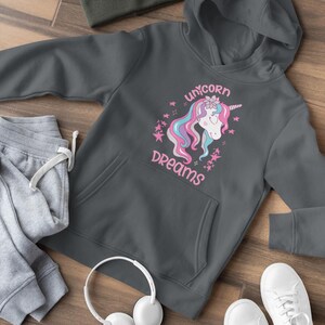 Könnte beinhalten: Ein anthrazitfarbener Hoodie mit einem rosa Einhorn-Motiv und dem Text "unicorn dreams". Der Hoodie hat eine Kapuze mit Kordelzug und eine Kängurutasche.