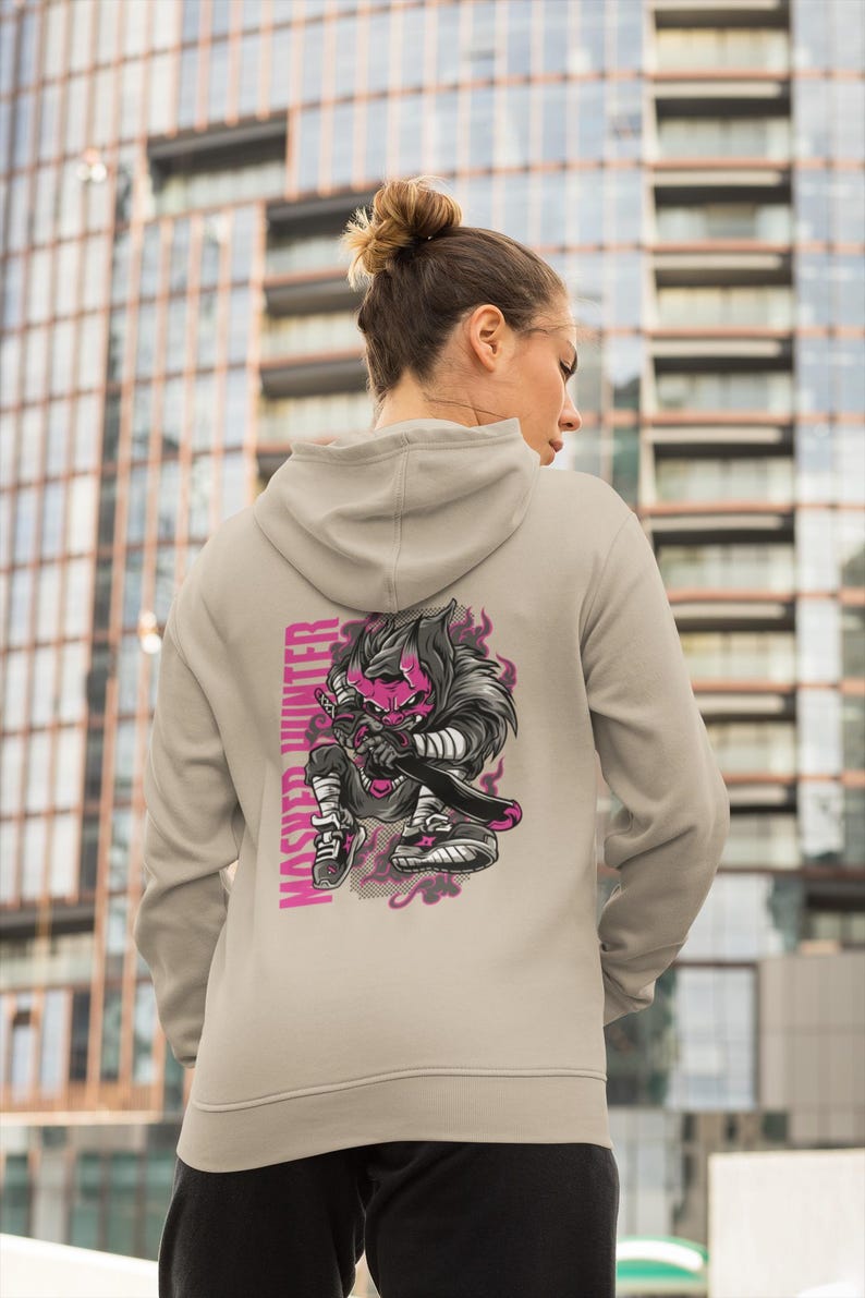 May include: A beige hooded sweatshirt featuring a graphic print on the back. The design depicts a stylized character with a pink face and dark hair holding a sword, accompanied by the vertical text "MASHER HUNTER" in bold pink capital letters.