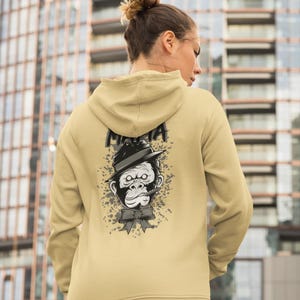May include: A beige hooded sweatshirt featuring a graphic print on the back. The design displays a grayscale illustration of a gorilla wearing a fedora hat and a bow tie, with a cigar in its mouth. The word "MAFIA" is printed above the gorilla.