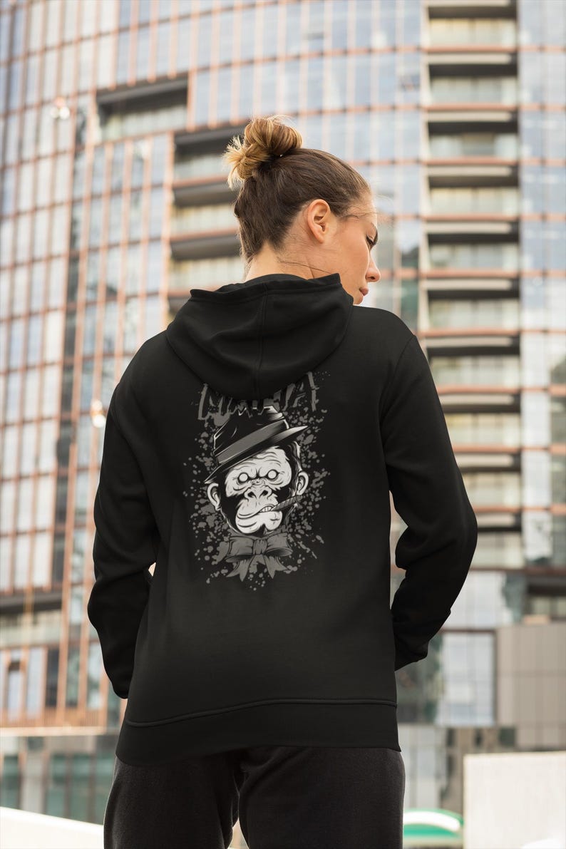May include: A black hooded sweatshirt featuring a graphic print on the back. The design displays a grayscale illustration of a gorilla wearing a fedora hat and a bow tie, with a cigar in its mouth, surrounded by a splattered ink effect.