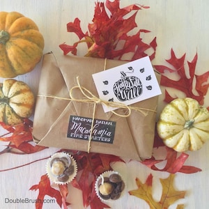 Pu&ograve; includere: Un pacco di carta marrone legato con spago ed etichettato "Handmade Natural Macadamia Fire Starters". Il pacco &egrave; circondato da foglie autunnali e piccole zucche. Un biglietto bianco con il testo "Happy Fall Y'all" &egrave; sopra il pacco.