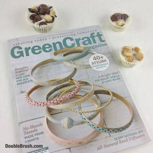 Pu&ograve; includere: Una copertina di rivista che presenta una variet&agrave; colorata di braccialetti, con il titolo "GreenCraft" e lo slogan "Creare oggi, preservare domani". La copertina della rivista presenta anche un testo su braccialetti, nappe e diffusori di canna.