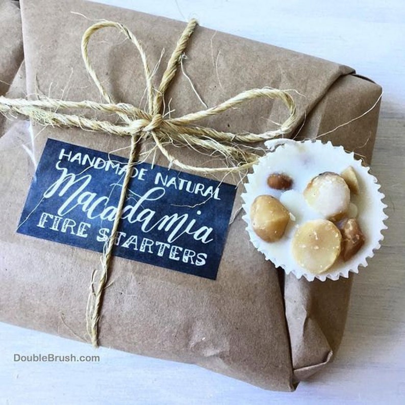 Pu&ograve; includere: Un pacco di carta marrone legato con spago ed etichettato "Handmade Natural Macadamia Fire Starters". Un accendino per camino a base di macadamia e cioccolato bianco &egrave; visibile in primo piano.