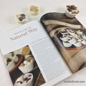 Pu&ograve; includere: Una pagina di rivista con il titolo "Accendere un fuoco in modo naturale" e una foto di caramelle di cioccolato bianco con noci e gocce di cioccolato. Le caramelle sono in piccoli bicchieri di carta bianca e sono disposte in cerchio su una superficie di legno.