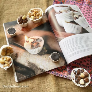 May include: A close-up of a magazine page featuring a variety of small white and brown candles with nuts and a wick. The candles are arranged on a wooden surface. The magazine page is open to an article about making candles.