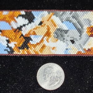 May include: A beaded bracelet with a colorful design of four horses. The horses are in a row, facing the same direction. The bracelet is made with small, colorful beads and has a gold clasp.