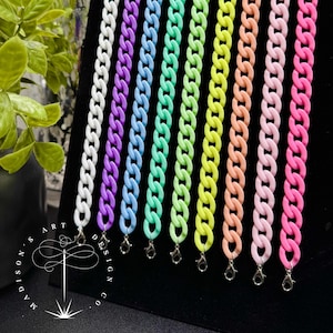 May include: A collection of nine acrylic chain straps in white, purple, blue, mint green, lime green, yellow, peach, light pink, and hot pink. Each chain features a silver-toned metal lobster clasp at the bottom end for secure attachment.