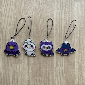 May include: Four cartoon character charms with black loops for attaching. The charms feature a purple duck, a white bear, a purple owl, and a purple character wearing a hat. The charms are on a light brown wooden surface.