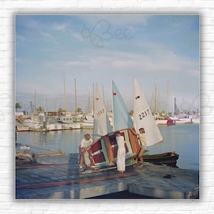 Stampa/poster Slim Aarons Sailing Dinghy - Un ragazzo e due ragazze che sollevano un canotto a vela dal suo rimorchio, San Diego, California Wall Photo