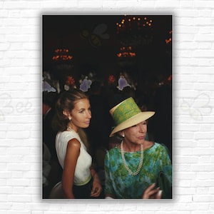 以下が含まれることがあります： 2 人の女性がテーブルに座っています。一人は緑と白の帽子をかぶっています。帽子をかぶった女性は、緑と青の模様のドレスに真珠のネックレスをしています。もう一人の女性は、白いノースリーブのトップスに真珠のネックレスをしています。