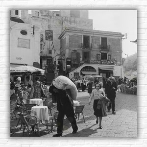 Stampa/poster di Slim Aarons, raffigurante una piazza cittadina italiana: un uomo che trasporta un sacco in una piazza affollata, Italia, circa 1949.