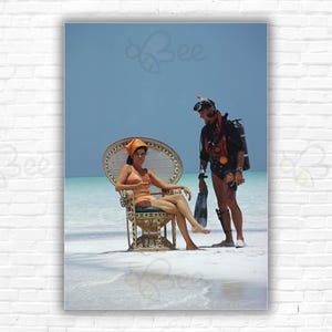 Slim Aarons A Friendly Chat Stampa/Poster - Un uomo che indossa attrezzatura subacquea parla con una ragazza su una sedia di vimini sulla spiaggia, Bahamas