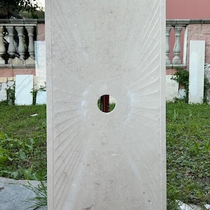 Puede incluir: Una losa rectangular grande de piedra de color gris claro con un recorte circular en el centro. La losa tiene un patrón decorativo radiante tallado en la superficie.